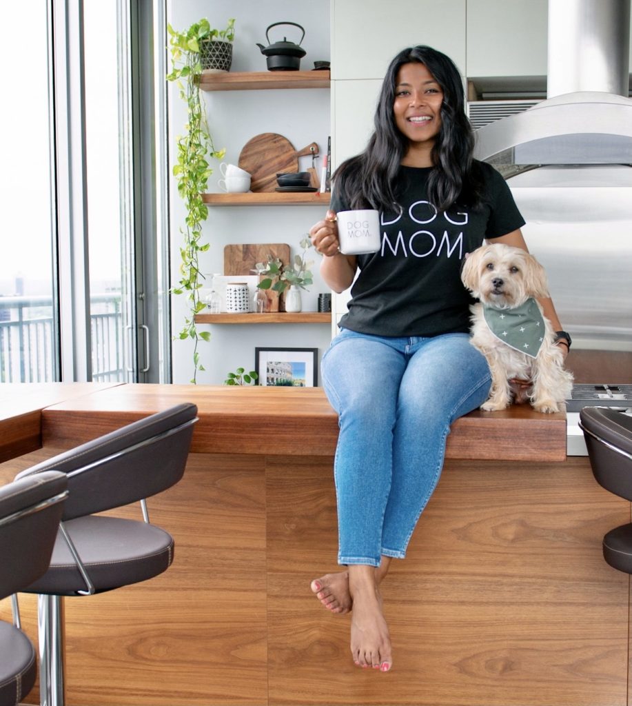 Sharon and Teddy are sitting on their kitchen counter. Sharon is wearing a dog mom shirt and holding a mug that says dog mom.