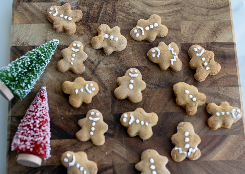 decorated gingerbread dog treats lay on a cutting board. 