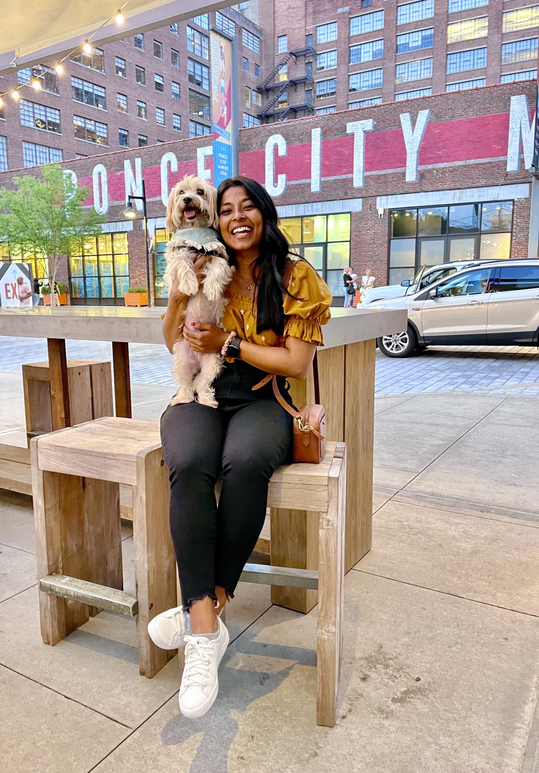 Sharon, a south east asian women has her small tan dog Teddy on her lap. They are sitting in front of a sign that says ponce city market.