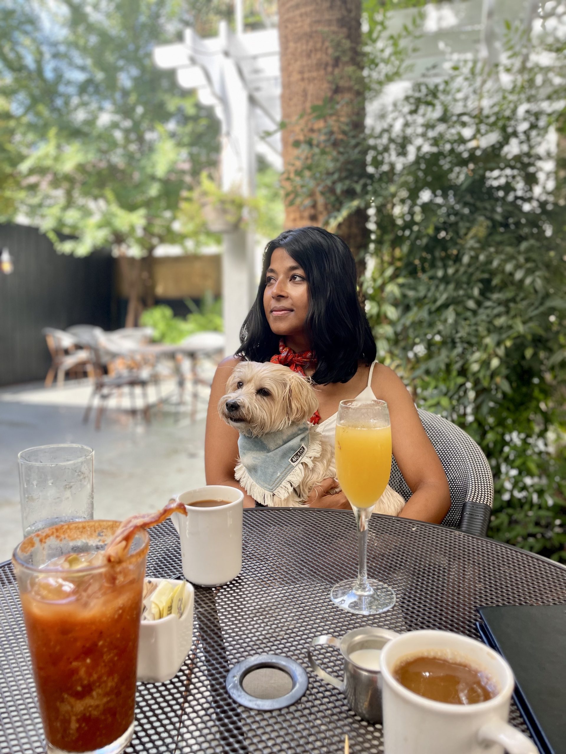 Sharon, a women of Indian descent sits with her small tan dog, Teddy on her lap at Eli's Table