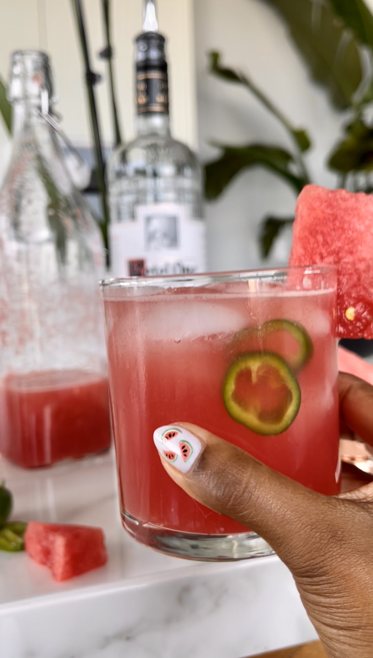 An Indian women is carrying a sparkling watermelon vodka drink with jalapeños. She has watermelons painted on her nails. 