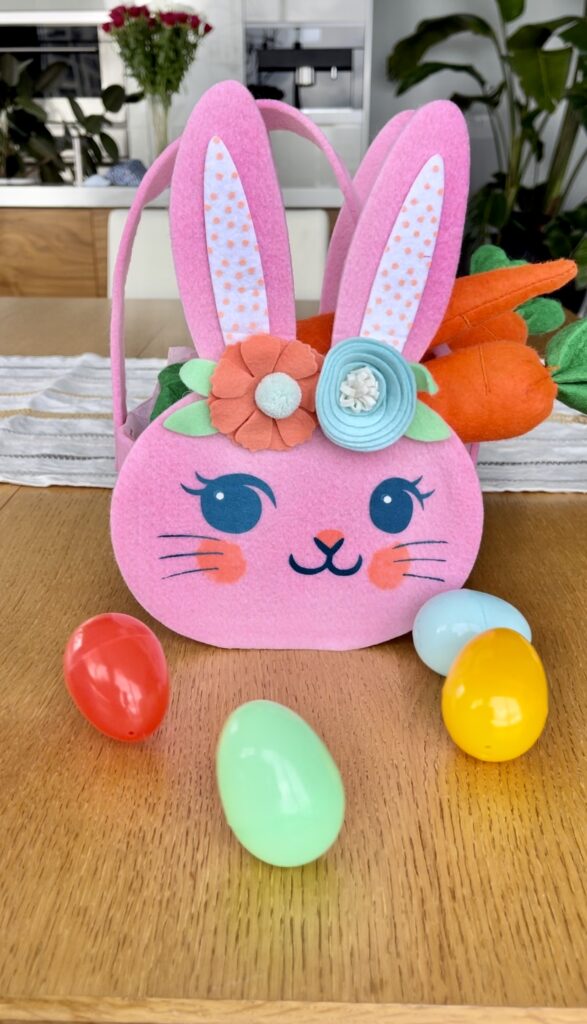 a pink bunny easter basket sits on a table with plastic eggs surrounding it
