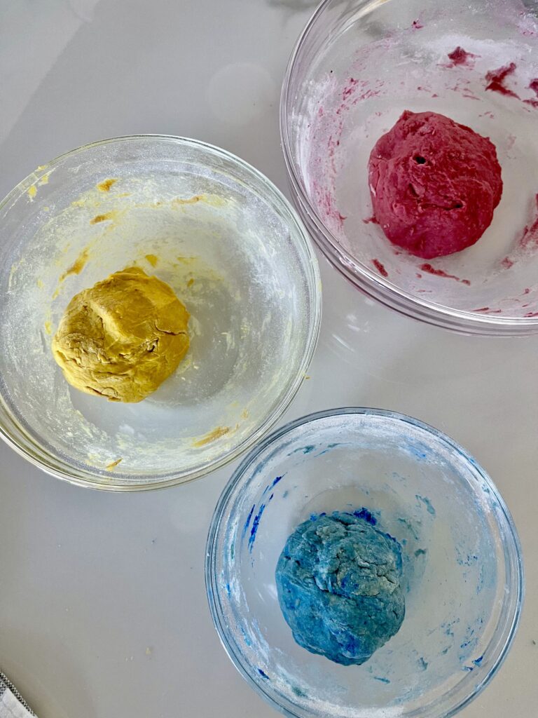 Red, yellow, and blue dyed dough sit in 3 bowls