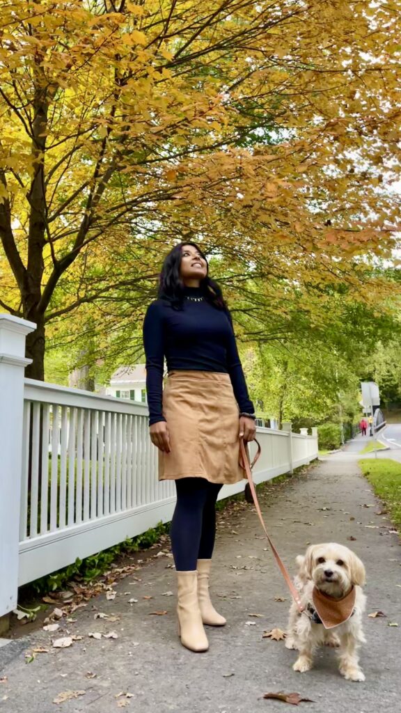 Sharon and her dog teddy stand in front of trees with beautiful yellow leaves in the town of Woodstock Vermont