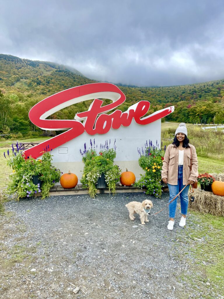 Sharon and her dog Teddy stand in front of a sign that says Stowe in Vermont